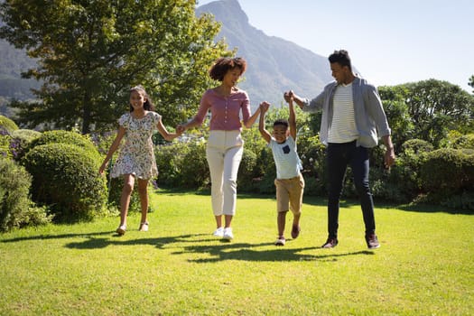 Happy african american couple with son and daughter outdoors, walking in sunny garden. family enjoying quality free time together.