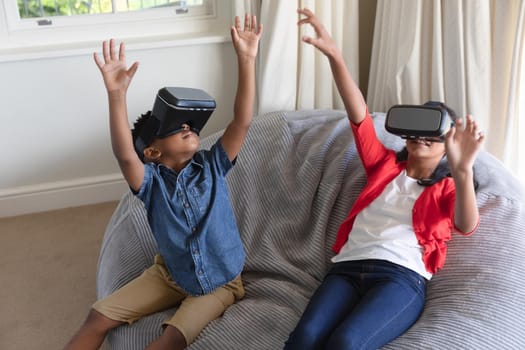 Happy african american boy and girl using vr headsets and smiling at home. childhood with technology, spending free time at home.