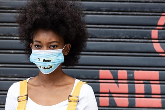 Portrait of mixed race woman wearing a face mask with writing. equal rights and justice protestors on demonstration march during coronavirus covid 19 pandemic.