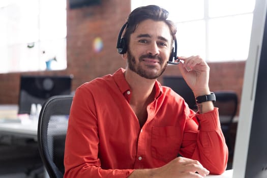 Portrait of caucasian businessman sitting at desk wearing headset having video call. independent creative design business.