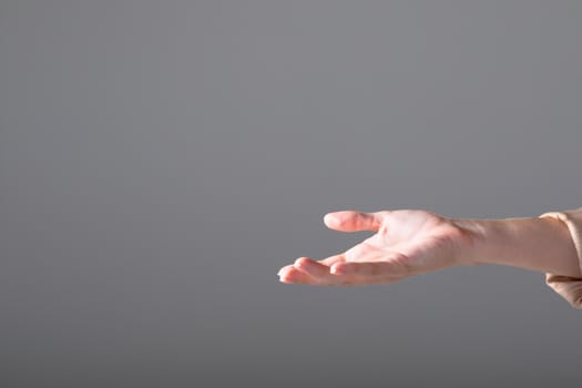 Midsection of caucasian businesswoman reaching with her hand, isolated on grey background. business, technology, communication and growth concept.