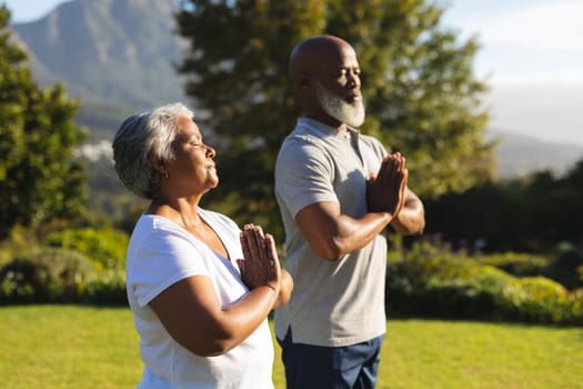 Senior african american couple meditating and practicing yoga with eyes closed in countryside. retirement and active senior lifestyle concept.