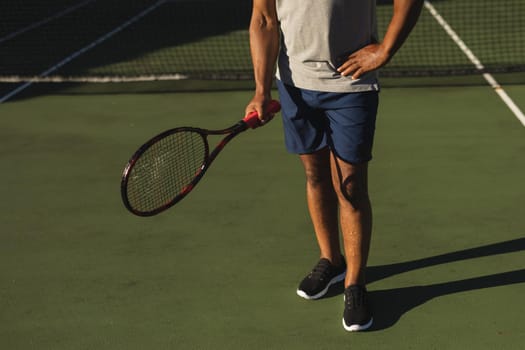 Midsection of senior african american man holding tennis racket on tennis court. retirement and active senior lifestyle concept.