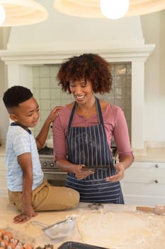 Happy african american mother with son baking in kitchen, using tablet. family enjoying quality free time together.