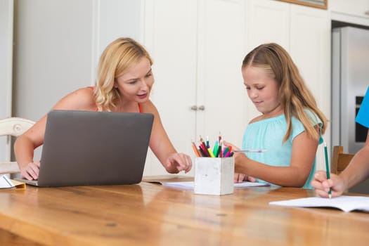 Caucasian mother using laptop and doing homework with her daughter smiling at home. family domestic life, spending time learning together at home.