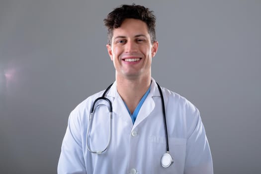 Portrait of caucasian male doctor looking at camera smiling, isolated on grey background. medical and healthcare services concept digitally generated composite image.