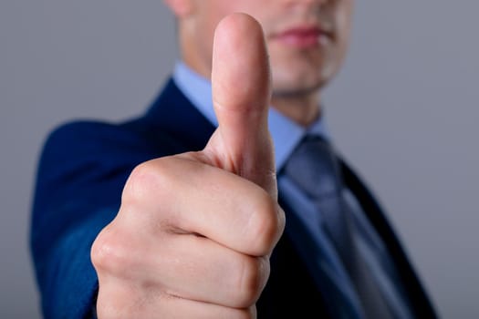 Midsection of caucasian businessman with thumb up, isolated on grey background. business technology, communication and growth concept.