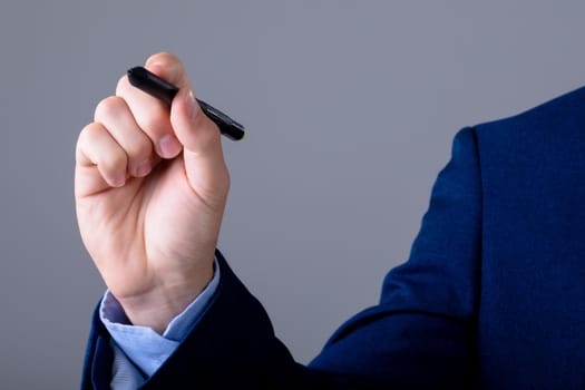 Midsection of caucasian businessman holding marker, isolated on grey background. business technology, communication and growth concept.