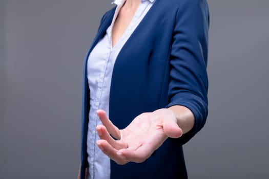 Midsection of caucasian businesswoman reaching with her hand, isolated on grey background. business technology, communication and growth concept digitally generated composite image.