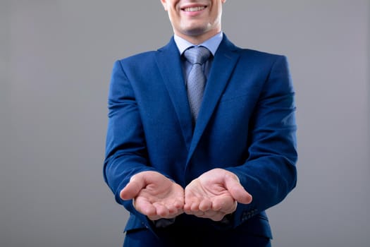 Smiling caucasian businessman showing his hands, isolated on grey background. business technology, communication and growth concept.