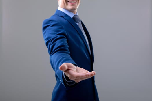 Smiling caucasian businessman reaching his hand, isolated on grey background. business technology, communication and growth concept.
