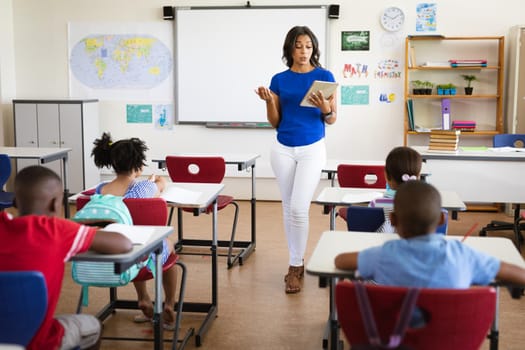 African american female teacher with digital tablet teaching in the class at elementary school. school and education concept