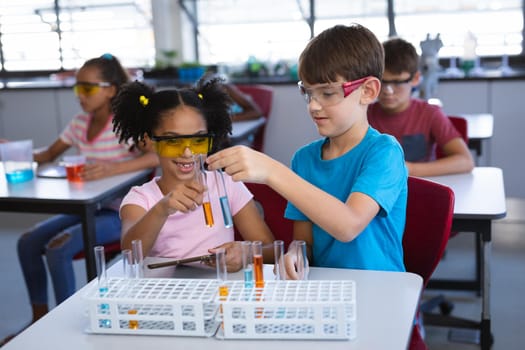African american girl and caucasian boy holding test tubes in science class at laboratory. school and education concept