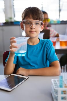 Portrait of caucasian boy holding a beaker filled with chemical in science class at laboratory. school and education concept