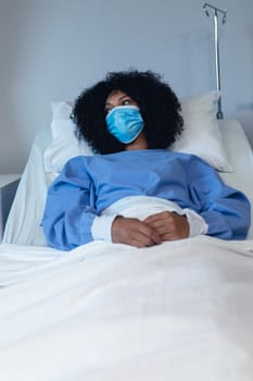 African american female patient lying in hospital bed wearing face mask. medicine and health services during coronavirus covid 19 pandemic.