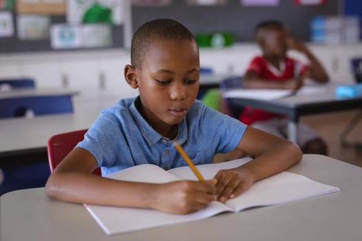 African american boy studying while sitting on his desk in the class at school. school and education concept