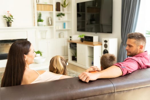 Caucasian couple with son and daughter sitting on couch watching television at home. domestic lifestyle and leisure family time concept.