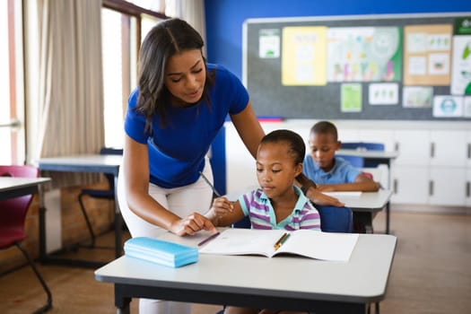 African american female teacher teaching african american girl in the class at elementary school. school and education concept