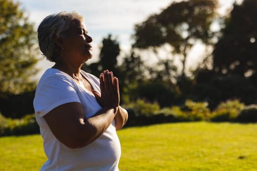 Senior african american woman with eyes closed practicing yoga in stunning countryside. retirement and active senior lifestyle concept.