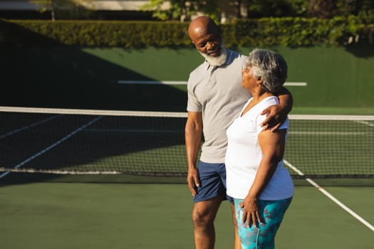 Portrait of smiling senior african american couple embracing on tennis court. retirement and active senior lifestyle concept.