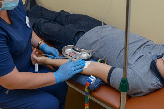 nurse in a blue uniform puts the patient medical drip into a vein.