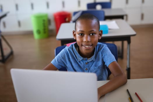 Portrait of african american boy smiling while using laptop sitting on his desk at elementary school. school and education concept