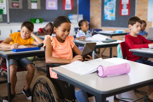 Disabled african american girl using digital tablet while sitting on wheelchair at elementary school. school and education concept