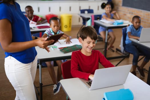 Mid section of female teacher teaching caucasian boy to use digital tablet at elementary school. school and education concept