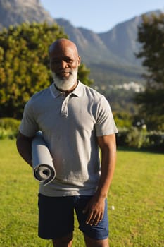 Portrait of smiling senior african american man with yoga mat in stunning countryside. retirement and active senior lifestyle concept.