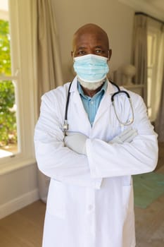 Portrait of senior african american male doctor in face mask and lab coat. retirement and senior lifestyle during covid 19 pandemic concept.