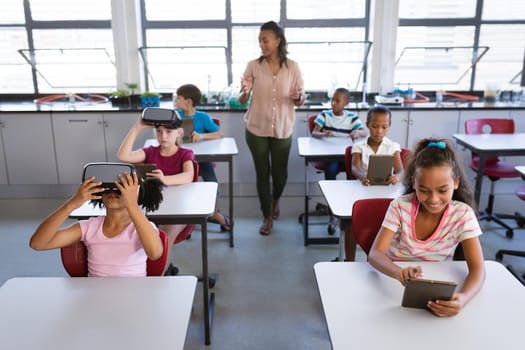 African american female teacher teaching students to use electronic devices in the class at school. school and education concept