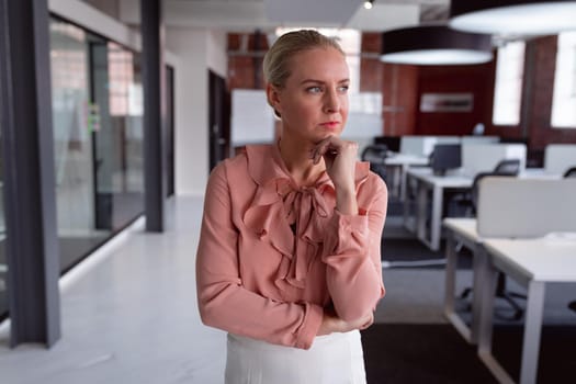 Thoughtful caucasian businesswoman standing in office with chin on hand, looking away. working in business at a modern office.