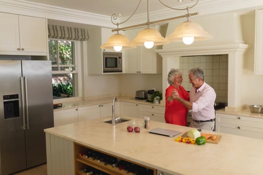 Senior caucasian couple dancing together and smiling in kitchen. retreat, retirement and happy senior lifestyle concept.