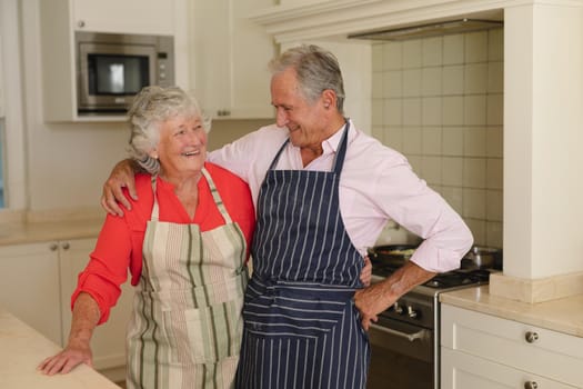 Senior caucasian couple embracing and smiling in kitchen. retreat, retirement and happy senior lifestyle concept.