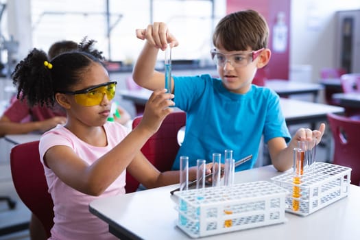 African american girl and caucasian boy holding test tube in science class at elementary school. school and education concept