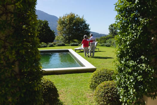 Senior caucasian couple embracing and walking in sunny garden. retreat, retirement and happy senior lifestyle concept.