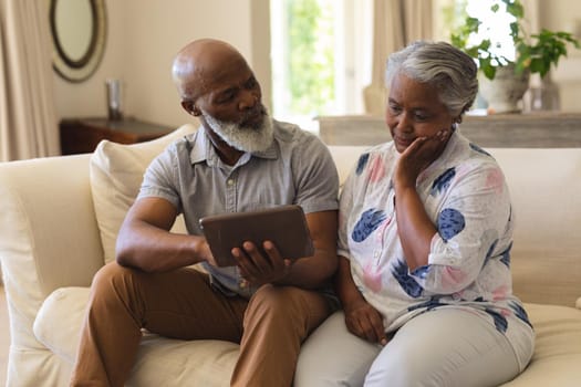 Senior african american couple sitting on sofa using tablet. retreat, retirement and happy senior lifestyle concept.