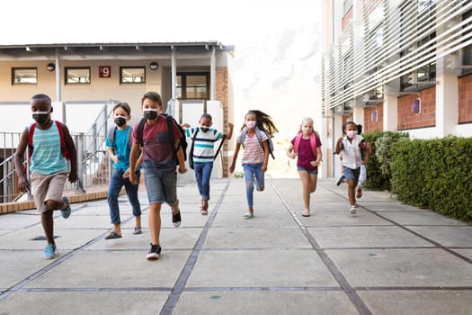 Group of diverse students wearing face masks running at elementary school. education back to school health safety during covid19 coronavirus pandemic.