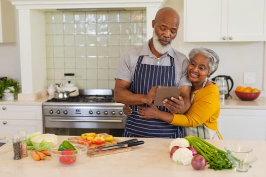 Senior african american couple cooking together in kitchen using tablet. retreat, retirement and happy senior lifestyle concept.