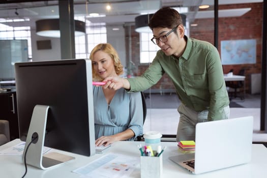 Happy diverse male and female colleague looking at computer screen and discussing at desk in office. working in business at a modern office.