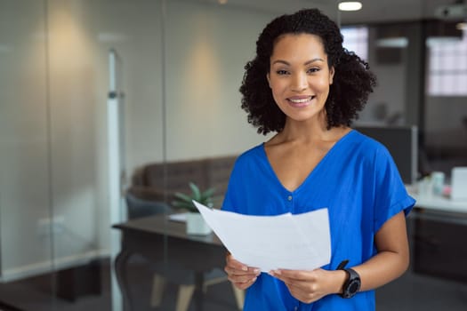 Portrait of smiling african american businesswoman holding paperwork standing in office. working in business at a modern office.