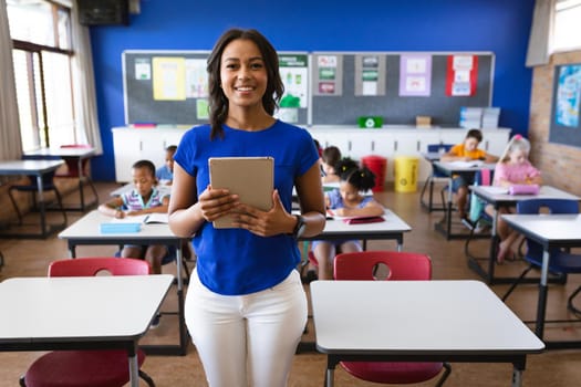 Portrait of african american female teacher holding digital tablet smiling in the class at school. school and education concept