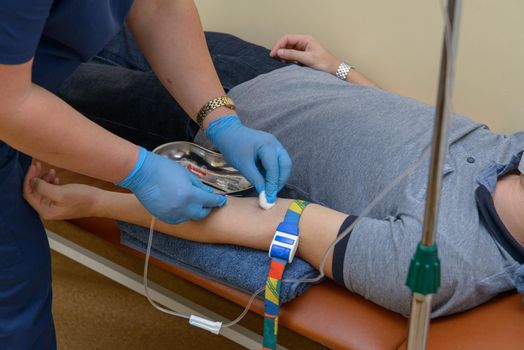 nurse in a blue uniform puts the patient medical drip into a vein.