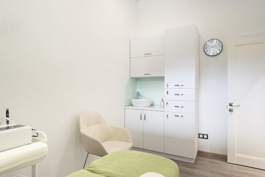 Beautiful interior of new salon, spa room, beauty parlour, or dermatological clinic with empty bed and modern skin care products on shelves and wall racks