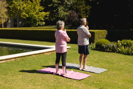 Senior caucasian couple practicing yoga, meditating in sunny garden. retirement retreat and active senior lifestyle concept.