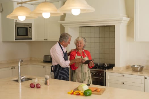 Senior caucasian couple using tablet together in kitchen. retreat, retirement and happy senior lifestyle concept.
