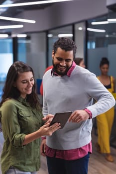 Two diverse creative colleagues using tablet and smiling. modern office of a creative design business.