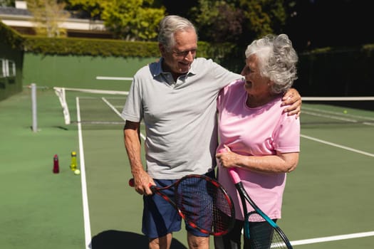 Senior caucasian couple embracing and smiling on tennis court. retirement retreat and active senior lifestyle concept.