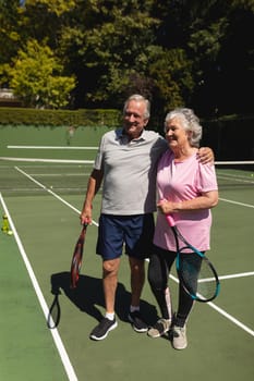 Senior caucasian couple embracing and smiling on tennis court. retirement retreat and active senior lifestyle concept.