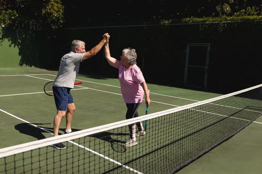 Senior caucasian couple playing tennis together on court highfiving. retirement retreat and active senior lifestyle concept.